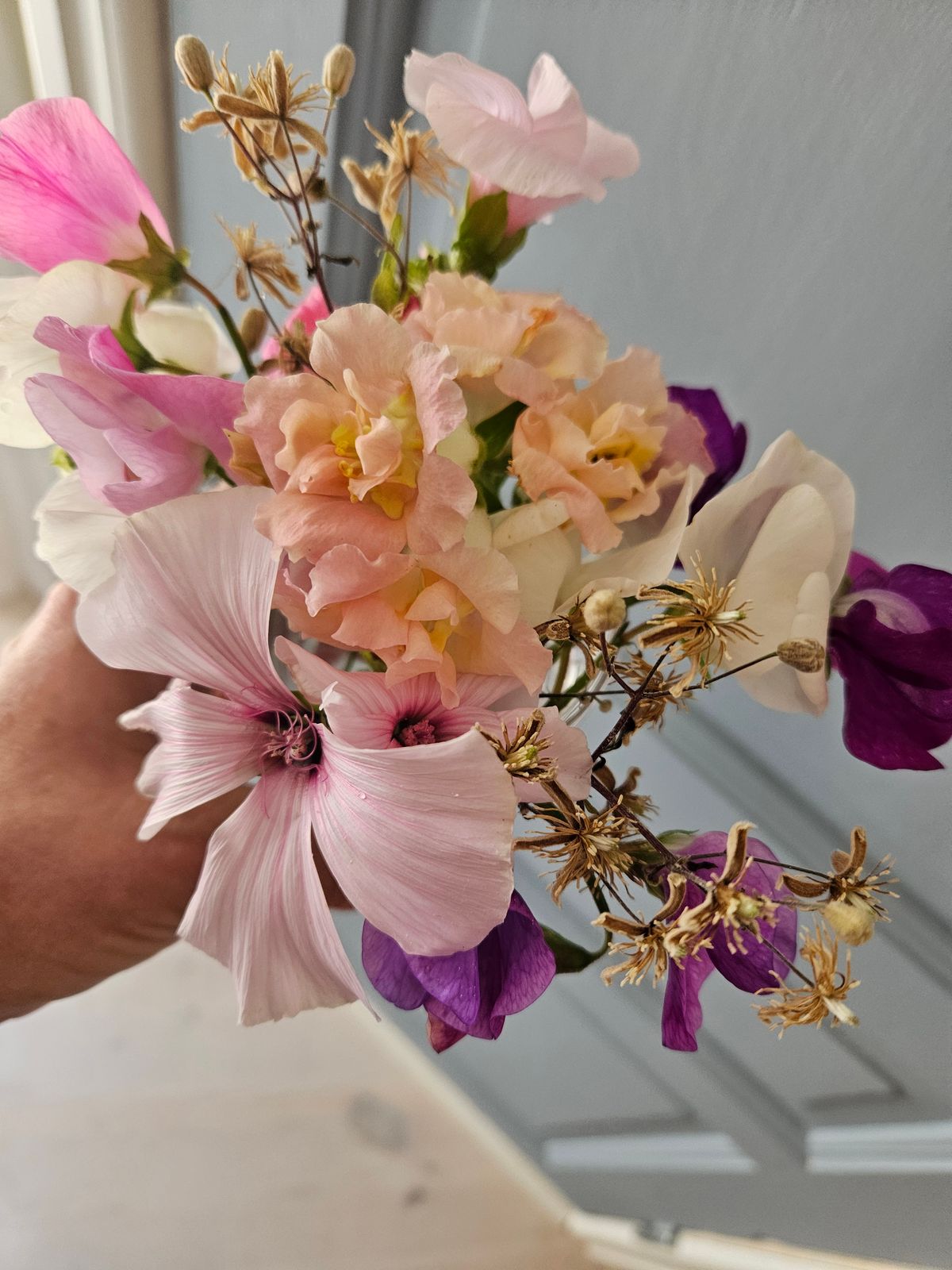 En handhållen bukett med rosa, vita och lila blommor samt några torra fröställningar.